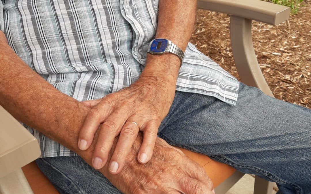 Warren's hands on lap wearing blue jeans and a plaid shirt